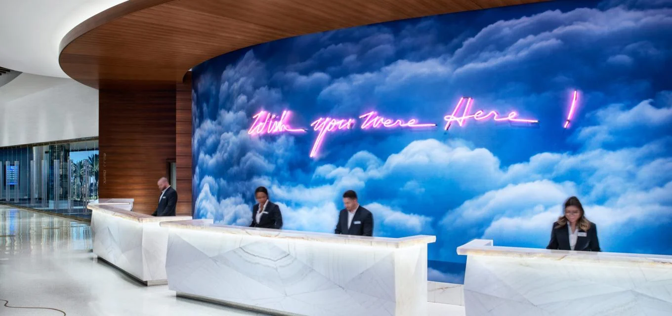 Palms hotel reception desk beneath a neon cloud mural reading ‘Wish you were here!’