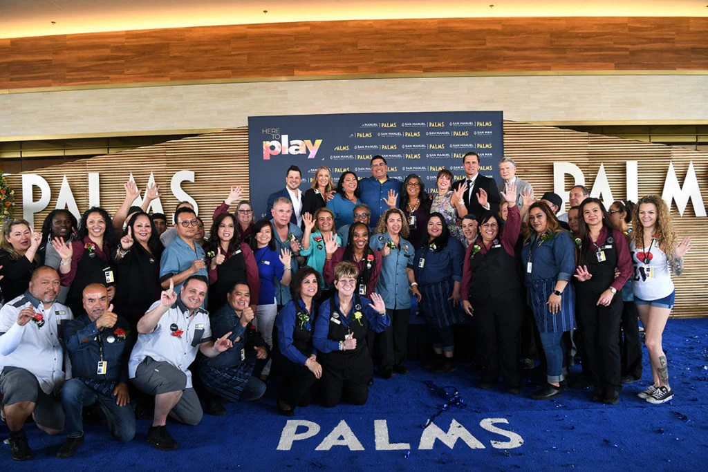 Group of Palms Team Members celebrating in front of a ‘Here to Play’ step-and-repeat backdrop