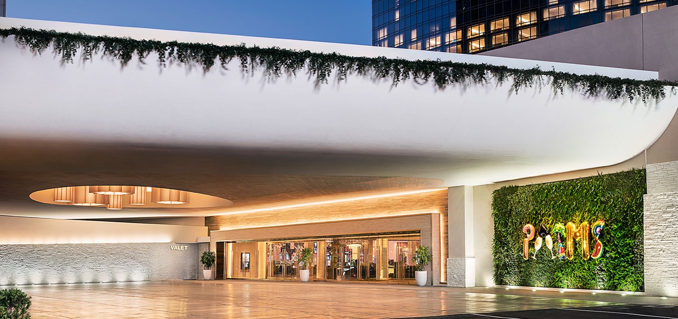 Valet entrance of the Palms Casino Resort in Las Vegas featuring a modern white overhang with greenery, illuminated glass doors, and a vibrant living wall with the Palms sign.